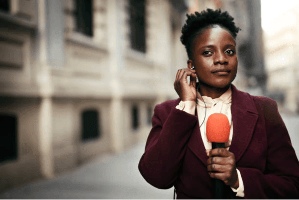 Person holding a microphone and wearing an earpiece on a city street.