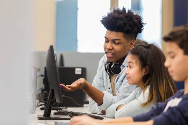 Students collaborating on a computer in a classroom setting, focused on the screen.