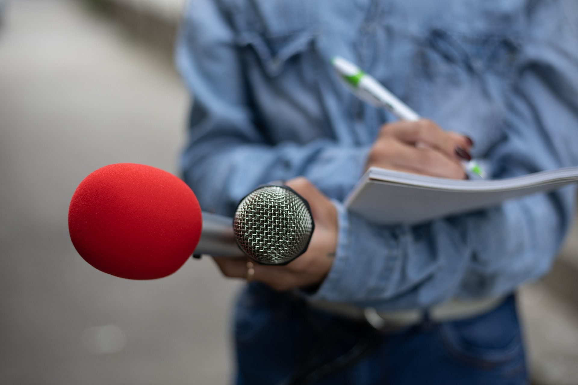 Journalist at news conference, writing notes, holding microphones
